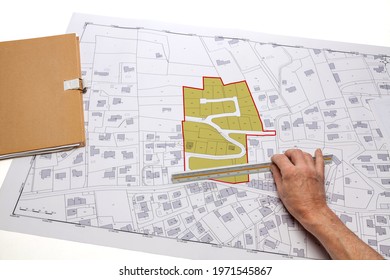 Town planning and land use planning - hand holding a measuring ruler in front of a zoning of plots, on a cadastral plan placed on a desk