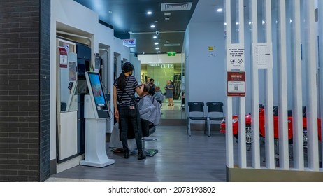 Townsville, Queensland, Australia - November 2021: Male Hairdresser In Shopping Center With Female Staff Cutting Hair Of Seated Male