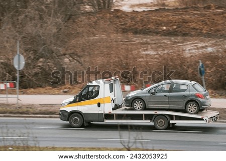 a towtruck is carrying a car that has broken down. The car has a problem with its engine and cannot be fixed on the spot. The tow truck service is delivering the car to a repair shop