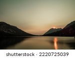 Toxaway Lake, an alpine lake in Idaho’s Sawtooth Wilderness seen on a summer day at dawn, with the sun rising over the mountains reflecting orange light in the surface of the water.