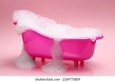 Toy bathtub overflowing with foam on pink background