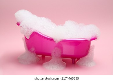 Toy bathtub overflowing with foam on pink background