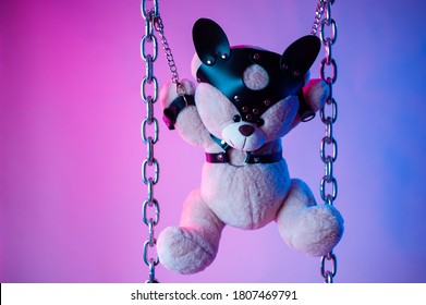 toy bear dressed in leather belts harness accessory for BDSM games on a dark background in neon light