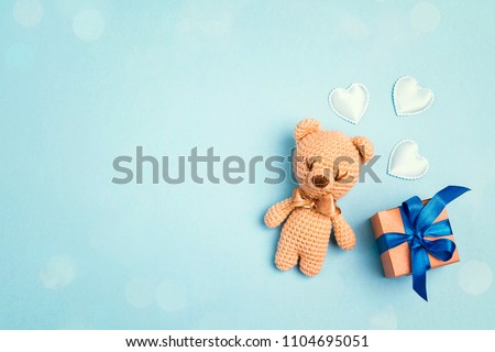 Toy bear and gift box on a blue background with copy space. Greting card concept. Top view, flat lay.