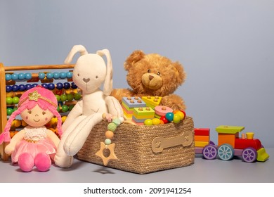 Toy box full of baby kid toys. Container with teddy bear, fluffy and educational wooden toys on light gray background. Cute toys collection for small children. Front view