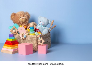 Toy box full of baby kid toys. Container with teddy bear, wooden rattles, stacking pyramid and wood blocks on light blue background. Cute toys collection for small children. Donation. Front view
