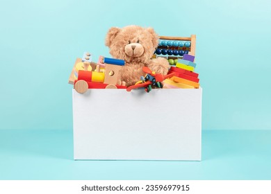 Toy box full of baby kid toys. Container with teddy bear, fluffy and educational wooden toys on light blue background. Cute toys collection for small children. Front view