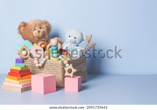 Toy box full of baby kid toys. Container with teddy\
bear, wooden rattles, stacking pyramid and wood blocks on light\
blue background. Cute toys collection for small children. Donation.\
Front view