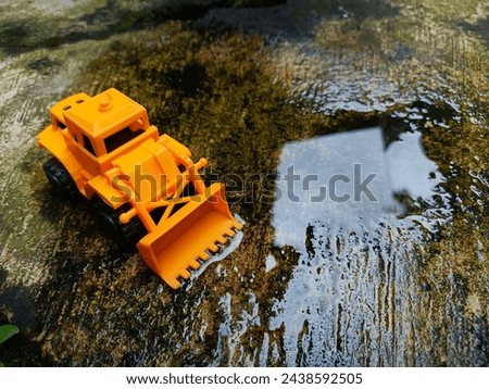 a toy bulldozer next to a puddle of rainwater