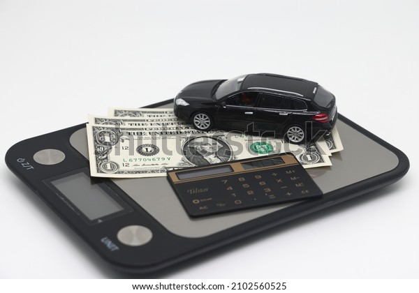 A toy car and\
banknotes lie on a kitchen electronic scale next to a calculator,\
the cost of operating a car.