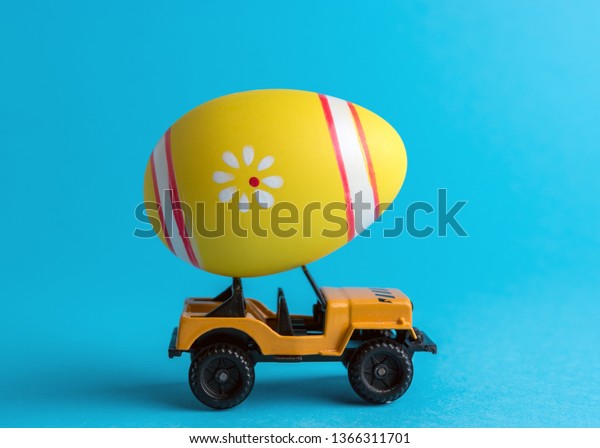 Toy car with colorful Easter egg on bright\
background. Minimal Easter\
concept.
