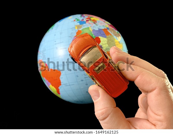 Toy car in hand on a\
background of the globe. Man with a car model, on a black\
background. A man points his hand to the globe. Concept: travel,\
tourism, geography