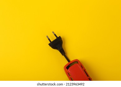 Toy car model with an electric plug on a yellow background. Electric car