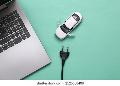 Toy car model with electric plug and laptop on blue background. Electric car