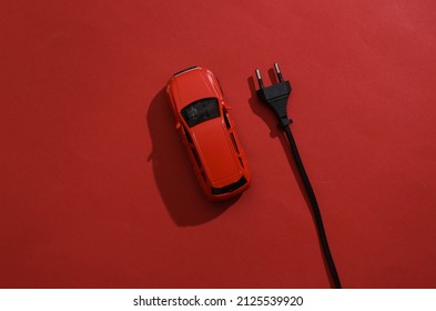 Toy car model with an electric plug on red background. Electric car