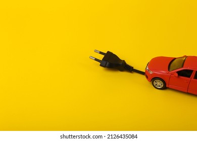 Toy car model with an electric plug on a yellow background. Electric car