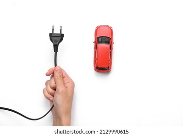 Toy car model with hand holding electric plug on a white background. Electric car