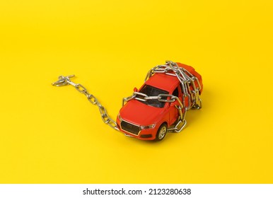Toy car model rewound by a steel chain on a yellow background. Driving license revocation concept