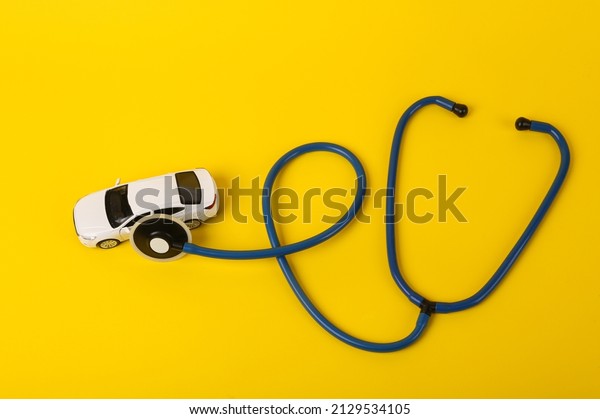 Toy\
car model with a stethoscope on a yellow background. Car breakdown\
diagnostics concept. Service center, auto\
workshop.