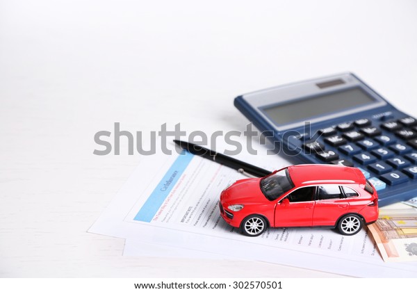 Toy car, money, documents and calculator on\
table. Car insurance\
concept