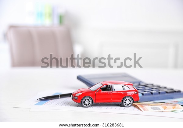 Toy car, money, documents and calculator on\
table. Car insurance\
concept