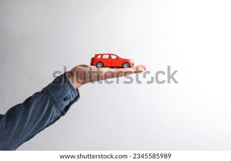 Toy car on Man's hand in denim shirt,  gray background.