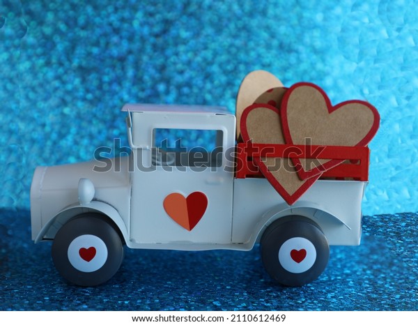 Toy car pick up truck with hearts in the
back. Truck is white with red hearts on the tires and door.  On a
pastel  blue sparkle background.

