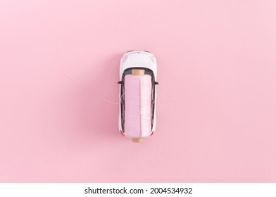 A Toy Car With A Thread And Needle On Pastel Pink Background. Flat Lay.