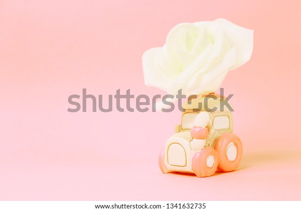 A Toy car with a white rose
on a pink background, the concept of holiday and gift, copy
space