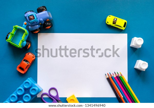 Toy cars, the designer, color\
pencils and a white sheet of paper on a blue background; concept of\
preschool education and development with space for\
copy\
