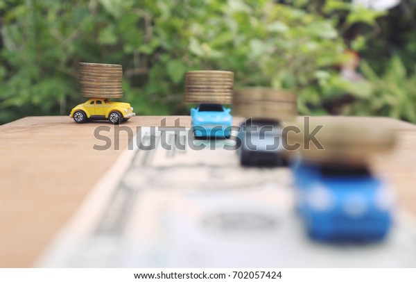 Toy cars help carry coins\
drive in line on blurred dollar money currency in natural garden\
and tree background, invest business and saving money concept      \
   
