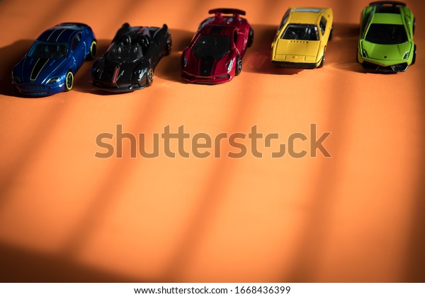 Toy cars lined up on an orange background\
with lines between them as if on a roadway.\
