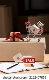 Toy Cart With Money, Gift Box And Credit Card On Notebook On Table