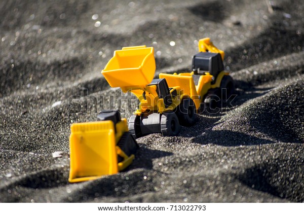 Toy construction\
machinery in black sand. Yellow and black colors toy machines.\
Bulldozer, loader,\
excavator.