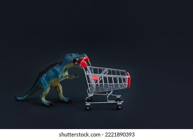 Toy dinosaur carries an empty shopping cart to the opening of store sales. Black Friday concept. Selective focus, copy space.