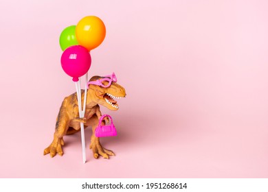 Toy dinosaur Tyrannosaurus with  holding colorful balloons in its paws on pink background Holiday card Happy women's, mother's day, birthday creative minimal concept 