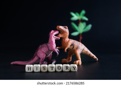 Toy Dinosaurs Next To The Cubes With The Inscription History. Studying Mesozoic Era And Ancient Reptiles. Educational Game About Extinct Animals. Black Background. Copy Space. Close-up