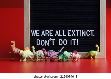 Toy dinosaurs next to a felt board that says We are all extinct. Don't do it! Red background. Concept agitating against self-destruction and extinction of mankind. Close-up