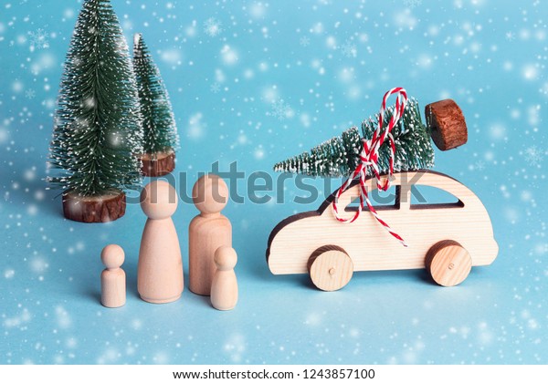 Toy family and toy car with Christmas tree on\
the roof. Wooden figures of father, mother and children who went by\
car to the forest for the Christmas tree. Symbolic concept of\
winter family holidays.