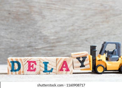 Toy forklift hold letter block y to complete word delay on wood background