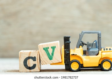 Toy forklift hold letter block V to complete word CV (Abbreviation of curriculum vitae) on wood background