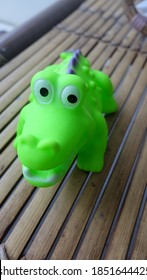 A Toy Green Aligator On The Bamboo Bench