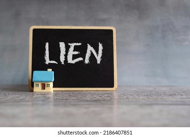 Toy House And Chalkboard With Text LIEN. Property And Real Estate Concept