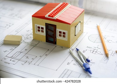 Toy house (constructor) on table with the drawings and business accessories