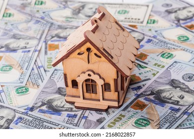 A toy house made of wood with a roof costs money, on a hundred-dollar bill. Concept: mortgage, purchase, sale of real estate, rental housing.
