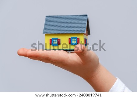 A toy house on a child’s palm, light background.