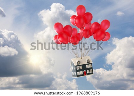 Toy house with red balloons floating in the blue sky with sunshine and white fluffy clouds. Soaring house princes and moving home concept