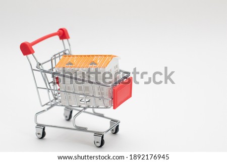 Toy house in a small shopping cart. Real estate concept.
