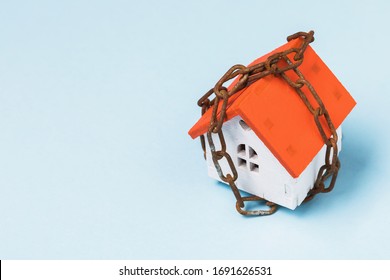 Toy House Wrapped In A Chain On A Blue Background With Copy Space. Property Arrest Concept