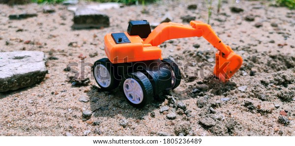 A toy JCB machine of a\
couple of inch is standing on sand and stone chips near a\
construction site.